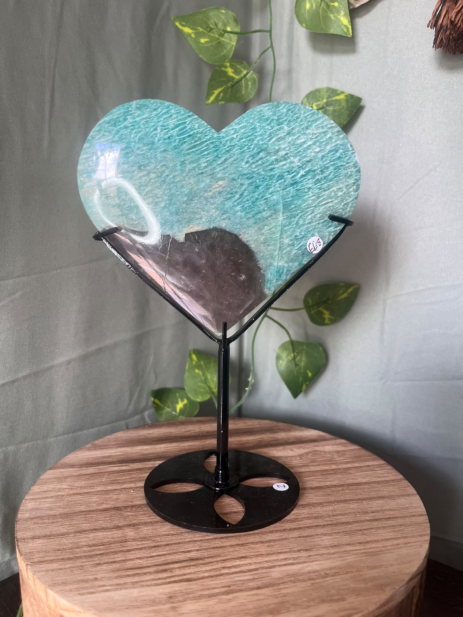 475g natural Amazonite heart crystal with Smoky Quartz matrix displayed on a black metal stand featuring vibrant turquoise-blue colouring.