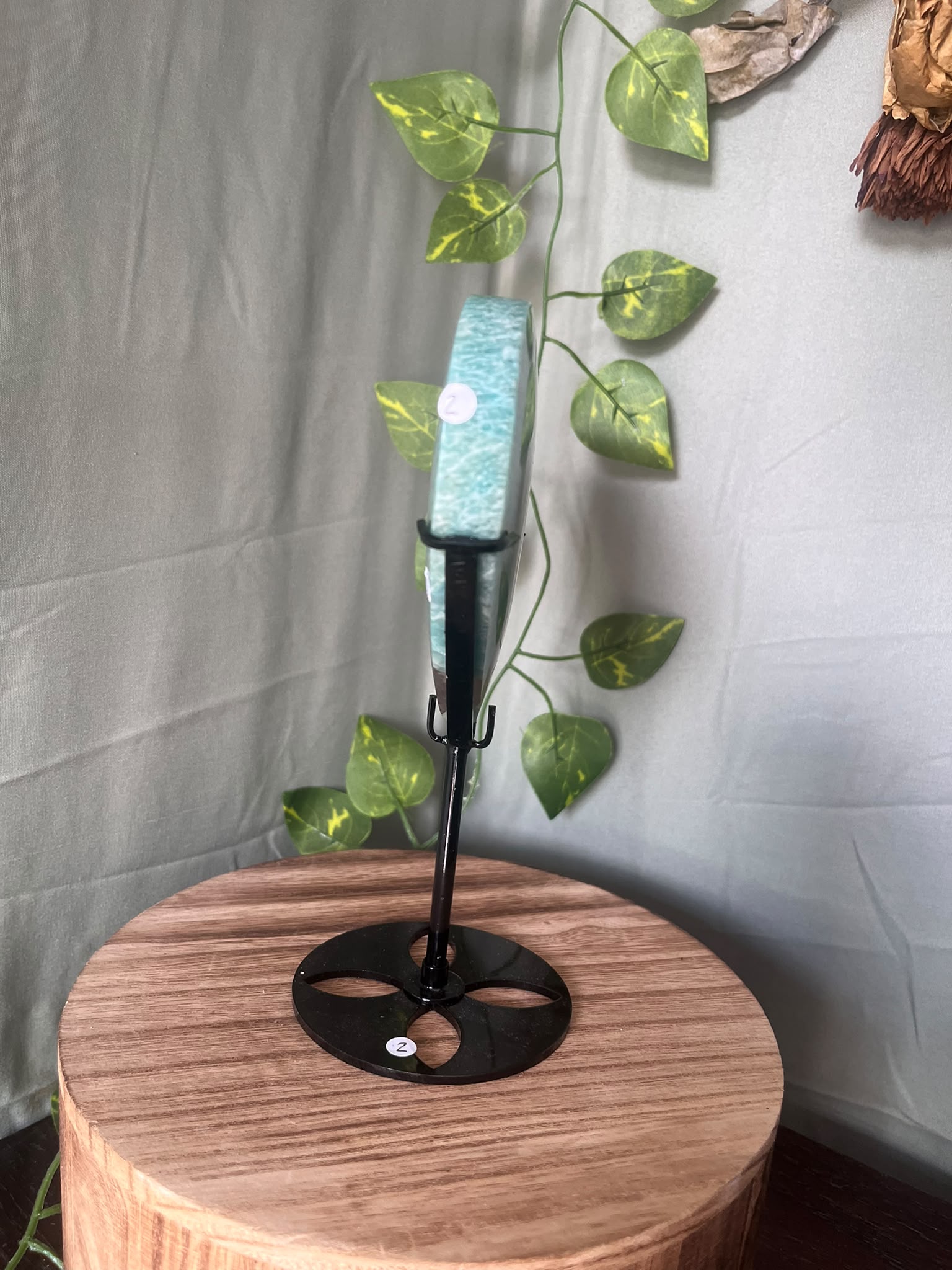 475g natural Amazonite heart crystal with Smoky Quartz matrix displayed on a black metal stand featuring vibrant turquoise-blue colouring.