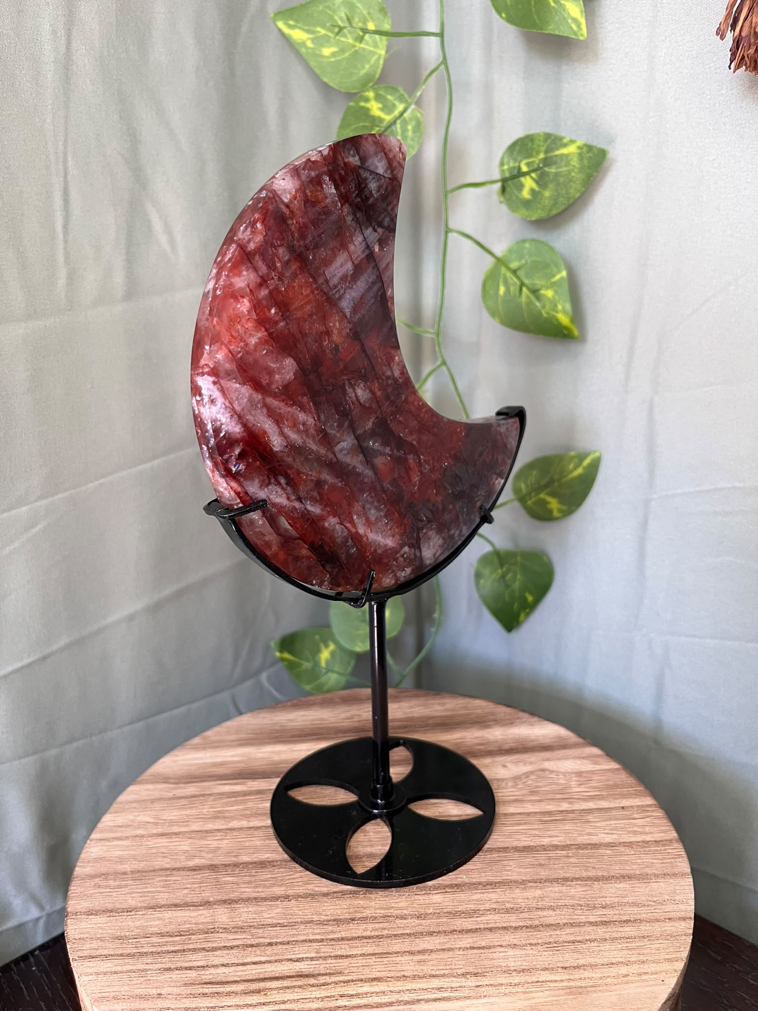 339g natural Fire Quartz crescent moon crystal carving displayed on a black metal stand with deep red hematite inclusions.