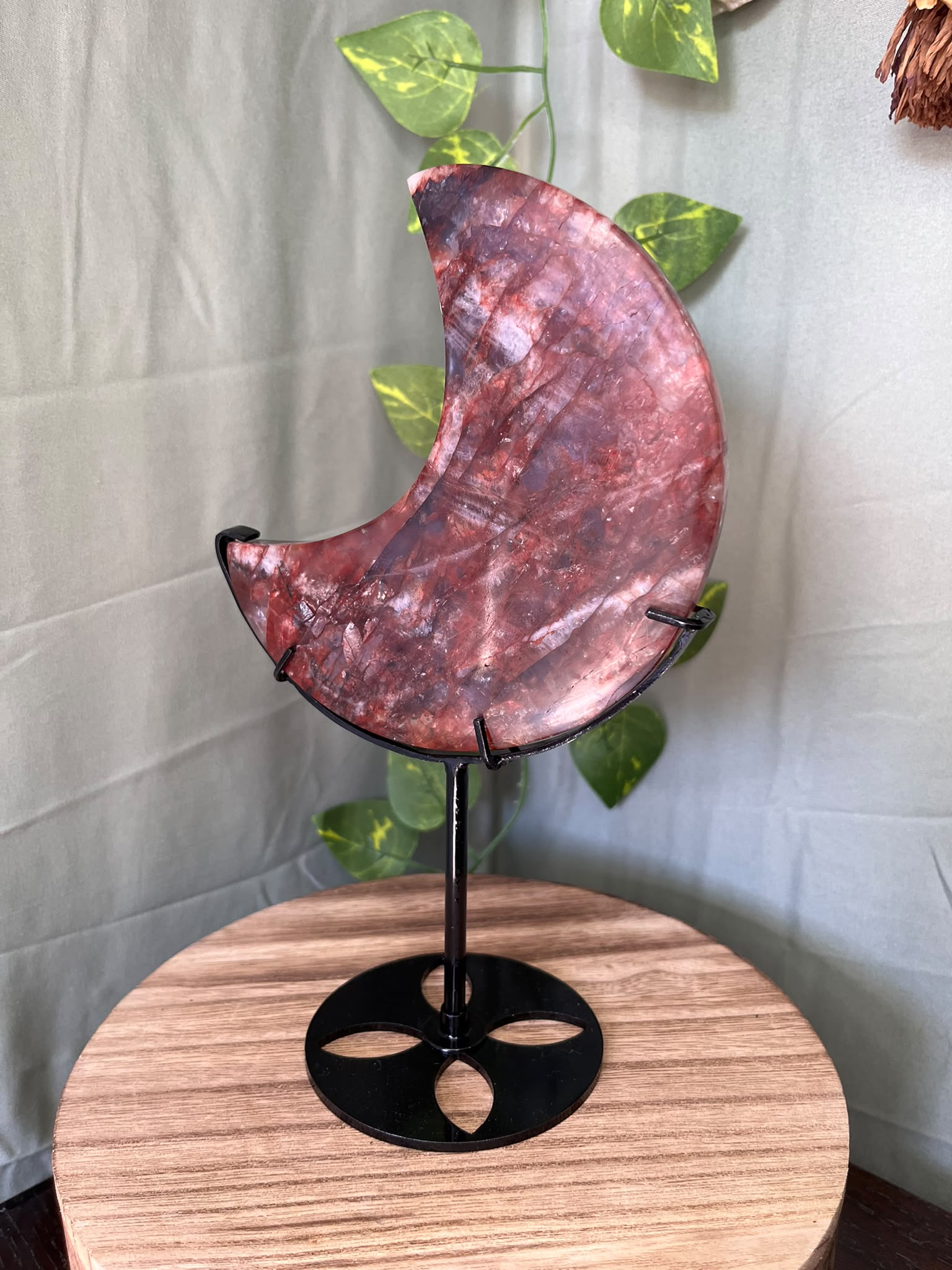 339g natural Fire Quartz crescent moon crystal carving displayed on a black metal stand with deep red hematite inclusions.
