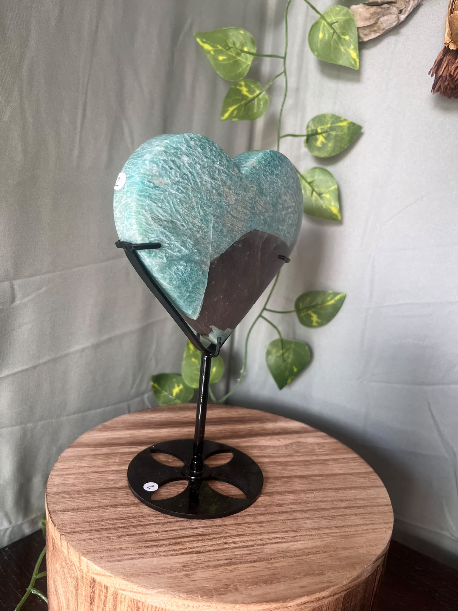 475g natural Amazonite heart crystal with Smoky Quartz matrix displayed on a black metal stand featuring vibrant turquoise-blue colouring.
