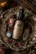 The Enchantress Ritual Anointing Oil displayed on an antique silver tray with dried roses, herbs and crystals, handcrafted for attraction, confidence and glamour magick.